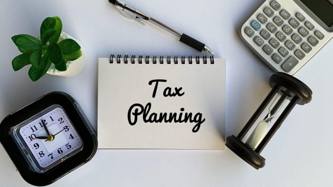 Tax planning text on notepad with calculator, clock and pen background. Business concept.